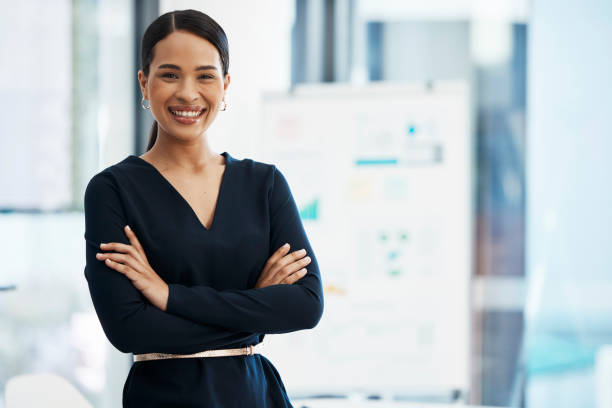 Confident, happy and smiling business woman standing with her arms crossed while in an office with a positive mindset and good leadership. Portrait of an entrepreneur feeling motivated and proud stock photo