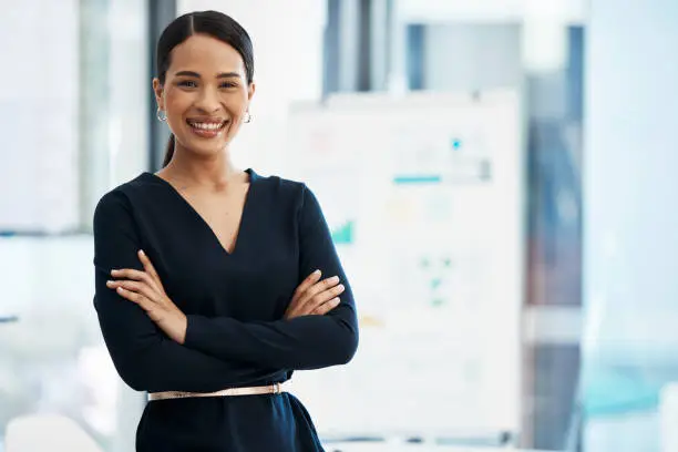 Photo of Confident, happy and smiling business woman standing with her arms crossed while in an office with a positive mindset and good leadership. Portrait of an entrepreneur feeling motivated and proud