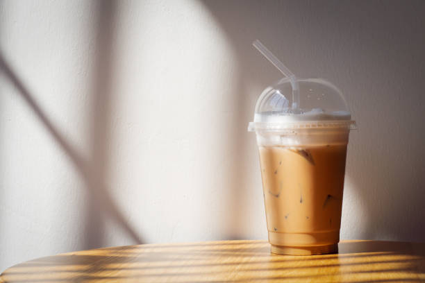 istock Ice cappuccino in plastic cup on wooden table. Shadow and warm light with copy space in warm color tone. 1426588042
