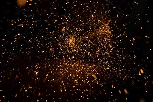 Sparks in dark. Lots of bright lights on black background. Burning metal particles fly in different directions. Industrial background.