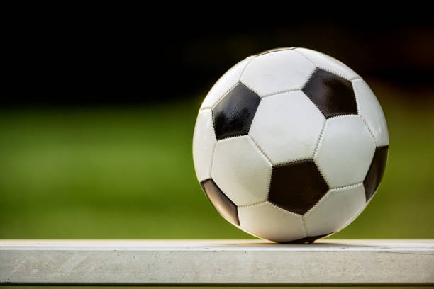A B&W soccer ball sitting on an aluminum bench at a sports field