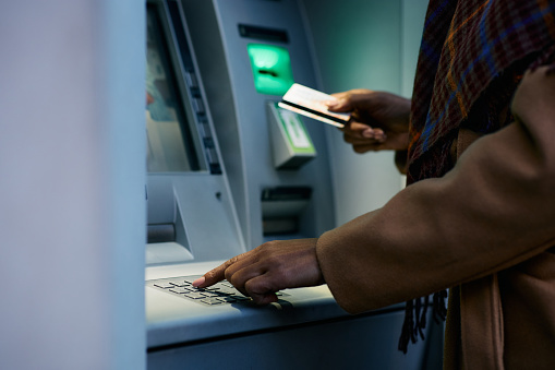 Close up of African American woman entering pin while using ATM machine.
