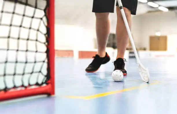 Floorball player. Floor hockey and indoor bandy game. White ball and stick. Goal and net on the floor in training arena. Young man or boy playing.