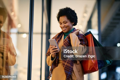 istock Happy black woman texting on cell phone while shopping in the city. 1426596365