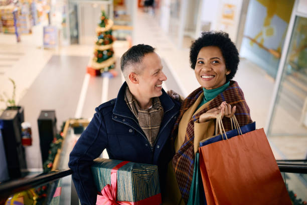 ショッピングモールでクリスマスショッピングを楽しんでいる幸せなカップル。 - spending money adult african ethnicity bag ストックフォトと画像