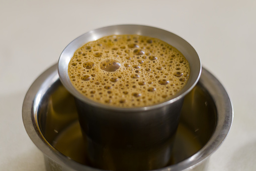south indian filter coffee served in traditional steel cup and saucer bowl. closeup shot of the popular frothy beverage with copy space.