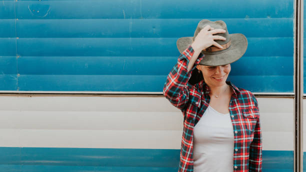 Woman in red checkered shirt, hat and blue background entering her trailer on a sunny afternoon
