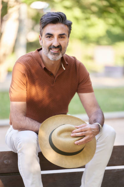 istock Relaxed middle-aged man looking at camera while sitting on a bench in a park. 1426606390