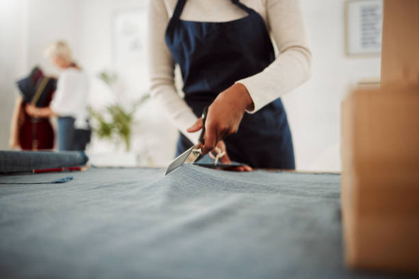 Fashion designer and tailor cutting fabric and making or preparing pattern for stylish, trendy and fashionable clothes. Workshop or boutique seamstress using denim material or textile for edgy wear