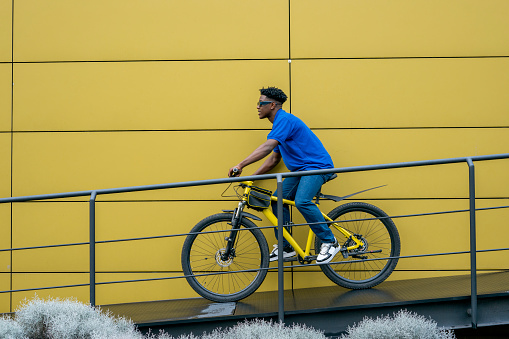 young man of average age of 25 years dressed comfortably black with afro hair is on the street with his yellow bicycle enjoying a sunny day