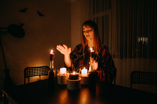 woman conjuring on candles during Halloween In a dark stylized room