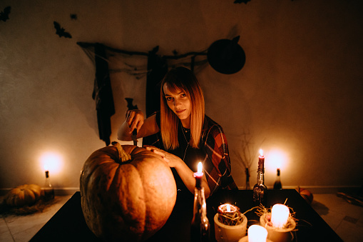 The woman carving pumpkin at the candles in the dark room. Halloween preparation