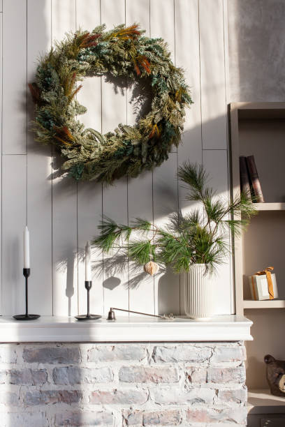 Modern stylish white interior with candles, vase with bouquet of pine branches and christmas wreath on the wall. stock photo