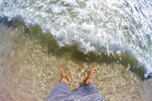 POV Point of view shot of a young latin man barefoot watching a wave over his foot in a paradise blue sea at South Beach