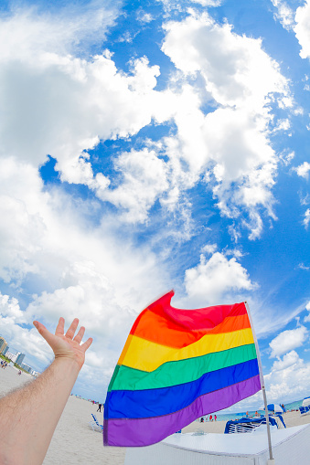POV Point of view shot of a young male having fun in South Beach, Miami Beach, Miami, South Florida, United States of America in front of a Gay Rainbow Flag in the Gay Beach Area.\n\nShooting from a personal perspective in an exotic tropical beach travel holidays.
