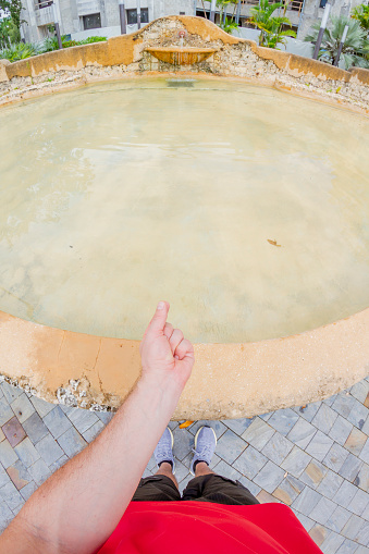 POV Point of view shot of a young male hand throwing Coin in Wishing Fountain in Coral Gables Area, Miami Beach, Miami, South Florida, United States of America.\n\nShooting from a personal perspective in an exotic tropical beach travel holidays.