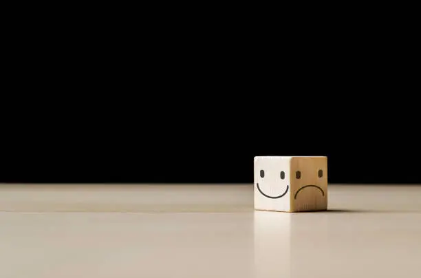 Photo of Smile face on the bright side and sad face in dark side on the wooden block cube for positive mindset selection. Mental health and emotional state concept, choice satisfaction feedback emotional.