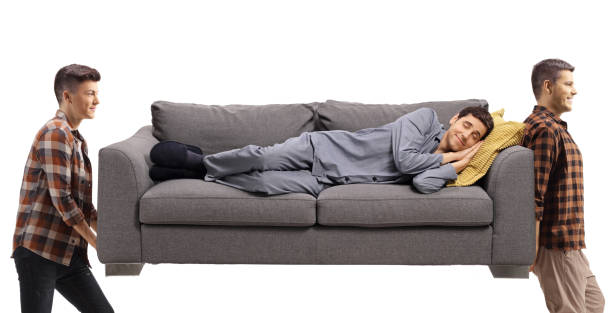 istock Man in pajamas sleeping on sofa and two young men carrying the sofa 1426626879