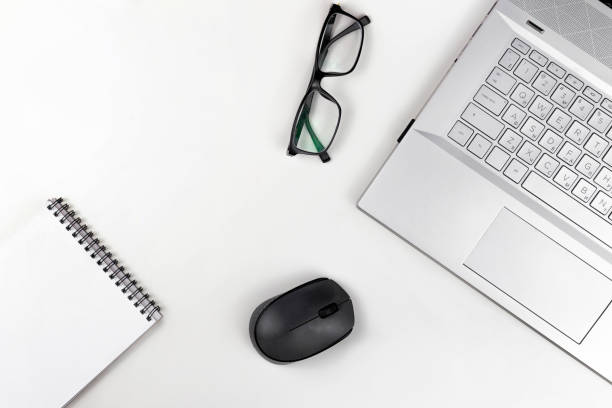 istock A blank notebook with glasses a computer mouse and a laptop are on a white table. Top view with copy space 1426627729