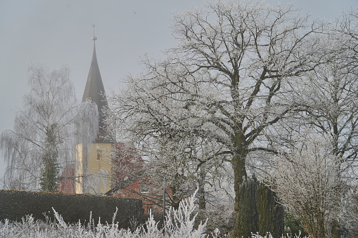 German church in a winter wonderland landscape with hoar frost on the church tower and a big tree
