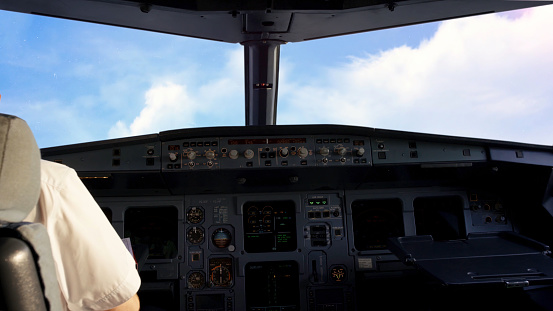 Pilot in the cockpit of a small commercial aircraft above a rural landscape, cloudy sky background. Pilots in the cockpit during a commercial flight.