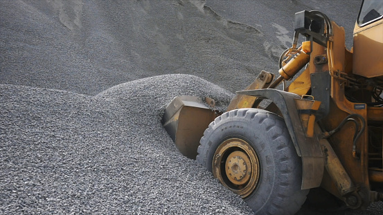 The tractor collects a scoop with gravel. Side view of an excavator loading its bucket with crushed stones or rubble at the construction site.