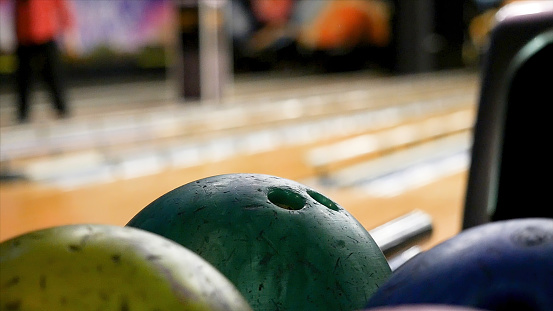 Close up for man hand taking a ball from a rack and throw it to the bowling lane. The player throws a bowling ball that knocks down and rolls.