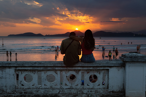 Santos, Brazil. February 20, 2022. Loving couple sitting on the wall in the city of Santos, Brazil, watching a sunset.