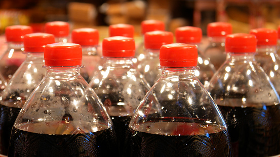 Many plastic bottles of cola with red caps close-up