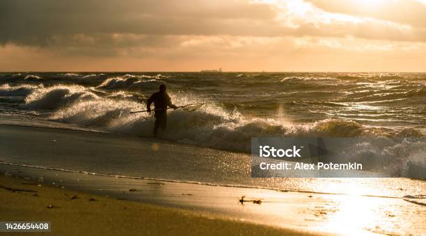 Man Wearing A Diving Suit Catching Amber In The Surf Of The Baltic Sea At Sunset Stock Photo - Download Image Now