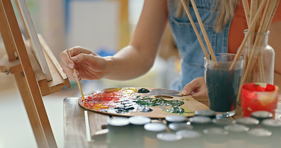 Artist, hands and watercolor paint on palette with brushes as painter starts oil painting alone in a workshop. Creative, talented and beginner learning drawing on a canvas in an art class or studio