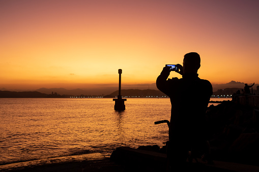 Santos, Brazil. May 22, 2022. Silhouette of tourists admiring the sunset at Ponta da Praia in Santos.