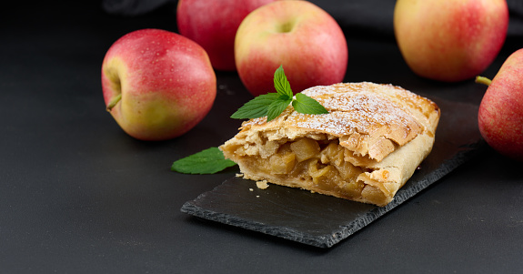 Baked strudel with apples sprinkled with powdered sugar on a black board