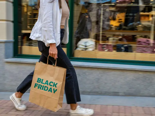 Photo of Moving image of a girl walking hurriedly with a shopping bag in front of a shop window. Shopping day, bargains, black friday.