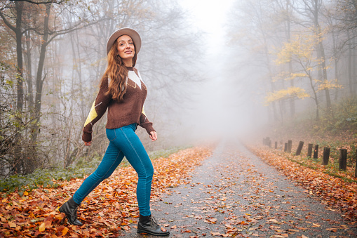 Woman walking on road at foggy autumn forest