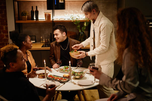 Young man putting vegetable salad on his plate while standing by dinner table