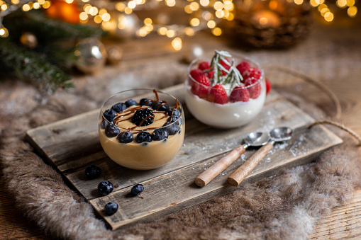 Christmas dessert crème caramel and Panna cotta with fresh berries in rustic wood kitchen and Christmas lights