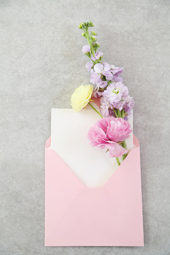 Top view of envelope and blank greeting card with flowers on pink background.