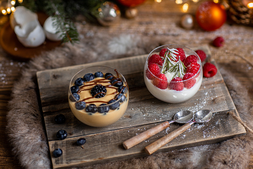 Christmas dessert crème caramel and Panna cotta with fresh berries in rustic wood kitchen and Christmas lights