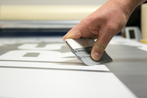 Close-up of a hand holding a trowel for making stickers. The person in the photo is just gluing the protective cover foil and pressing it.