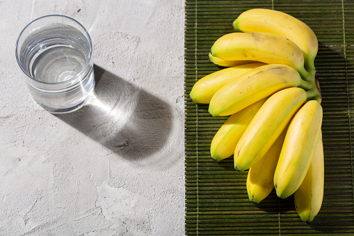 fresh bananas and glass with water, on the cement table, top view