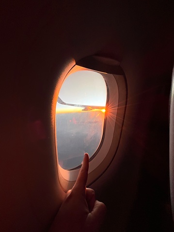 POV Point of view shot of a young male finger point inside an airplane in front of window, looking the sunset / sunrise on the horizon, waiting for his vacation time.