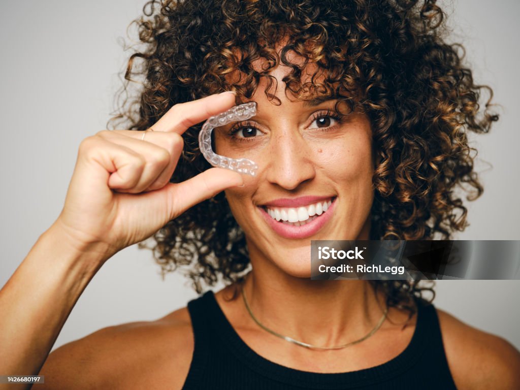 Smiling Woman Holding an Invisible Teeth Aligner A smiling woman holding an invisible teeth aligner. Dental Aligner Stock Photo