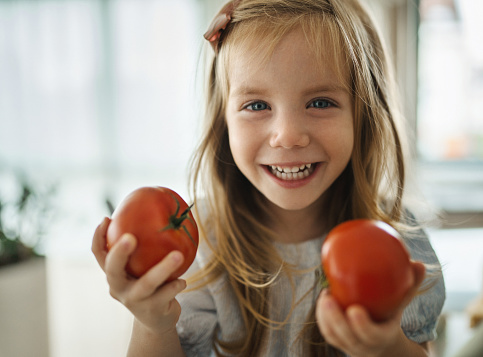 Closeup front view of a 3 year old girl holding couple of tomatoes and smiling to the camera.
