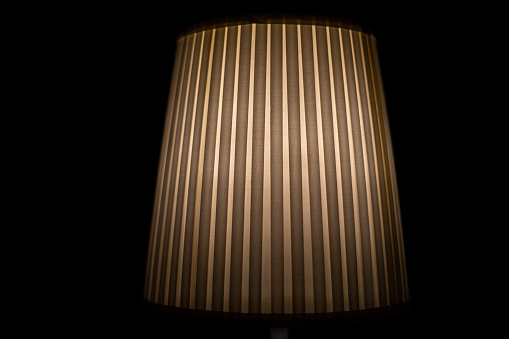 Lampshade lamp. Lamp is in dark. Light on black background. Ribbed paper. Interior item.