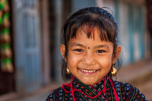Portrait of young Nepali girl posing in an ancient town of Bhaktapur. She is wearing tradittional Newari dress. Bhaktapur is an ancient town in the Kathmandu Valley and is listed as a World Heritage Site by UNESCO for its rich culture, temples, and wood, metal and stone artwork.
