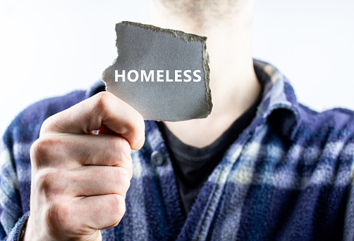 The man is holding a piece of paper with the word HOMELESS.The concept of asking for help from a homeless person.