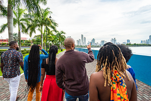 Local Tour Guide Showing a Point of Interest while Walking with a Group of Cheerful, Fashionable Afro-Descendant Black Young Men and Women Together with a View of Panama City, Panama from Plaza V Centenario