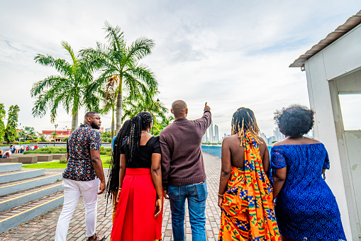 Local Tour Guide Pointing Forward While Walking with a Group of Cheerful, Fashionable Afro-Descendant Black Young Men and Women Together with a View of Panama City, Panama from Plaza V Centenario