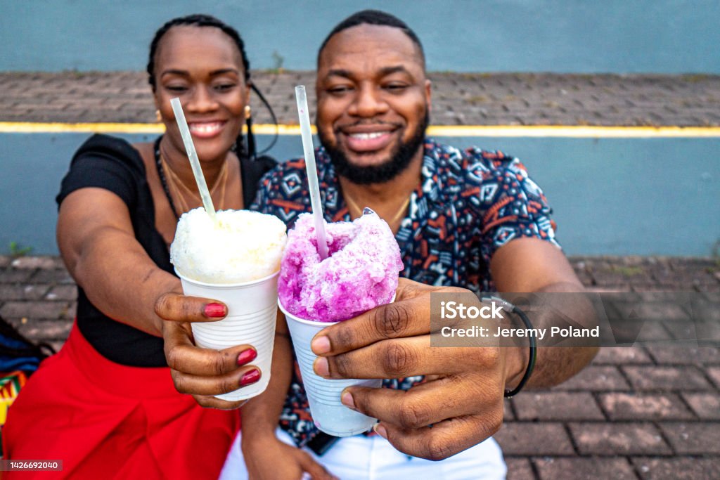 "Cheers!" Cute Portrait of an Afro-Descendant Friends Sitting Together and Holding "Raspao" Snow Cones at Plaza V Centenario in Panama City, Panama Cute Portrait of an Afro-Descendant Couple Sitting Together and Holding "Raspao" Snow Cones at Plaza V Centenario in Panama City, Panama 30-34 Years Stock Photo